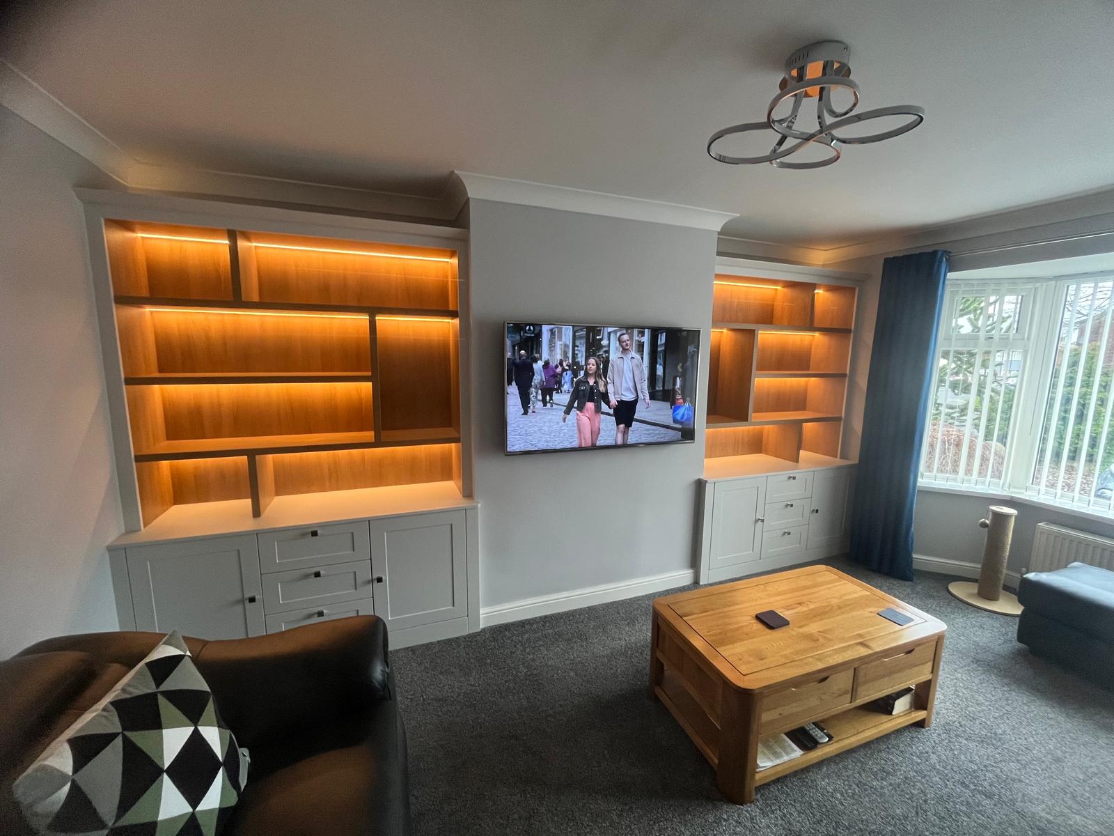 Bespoke fitted living room media unit with integrated shelving, warm LED lighting and TV wall installed by Bespoke Furniture Group in a Newcastle home